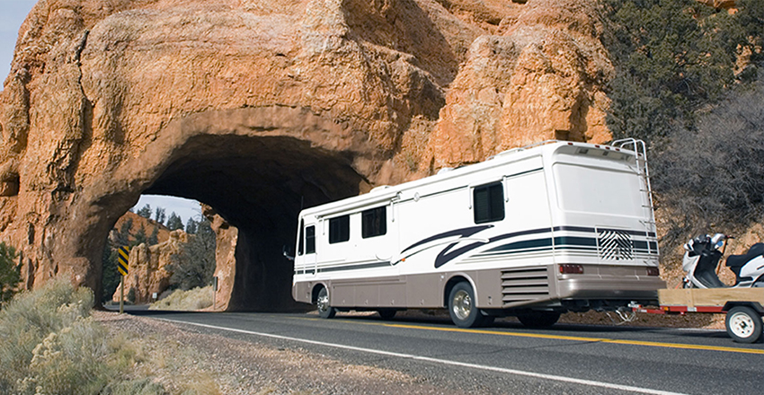 Back side view of an RV pulling a powersports vehicle in a trailer behind it