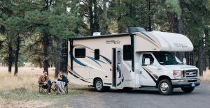 Two people sitting in folding chairs in front of an RV in the woods