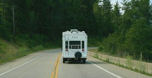The back of an RV driving down a road surrounded by trees