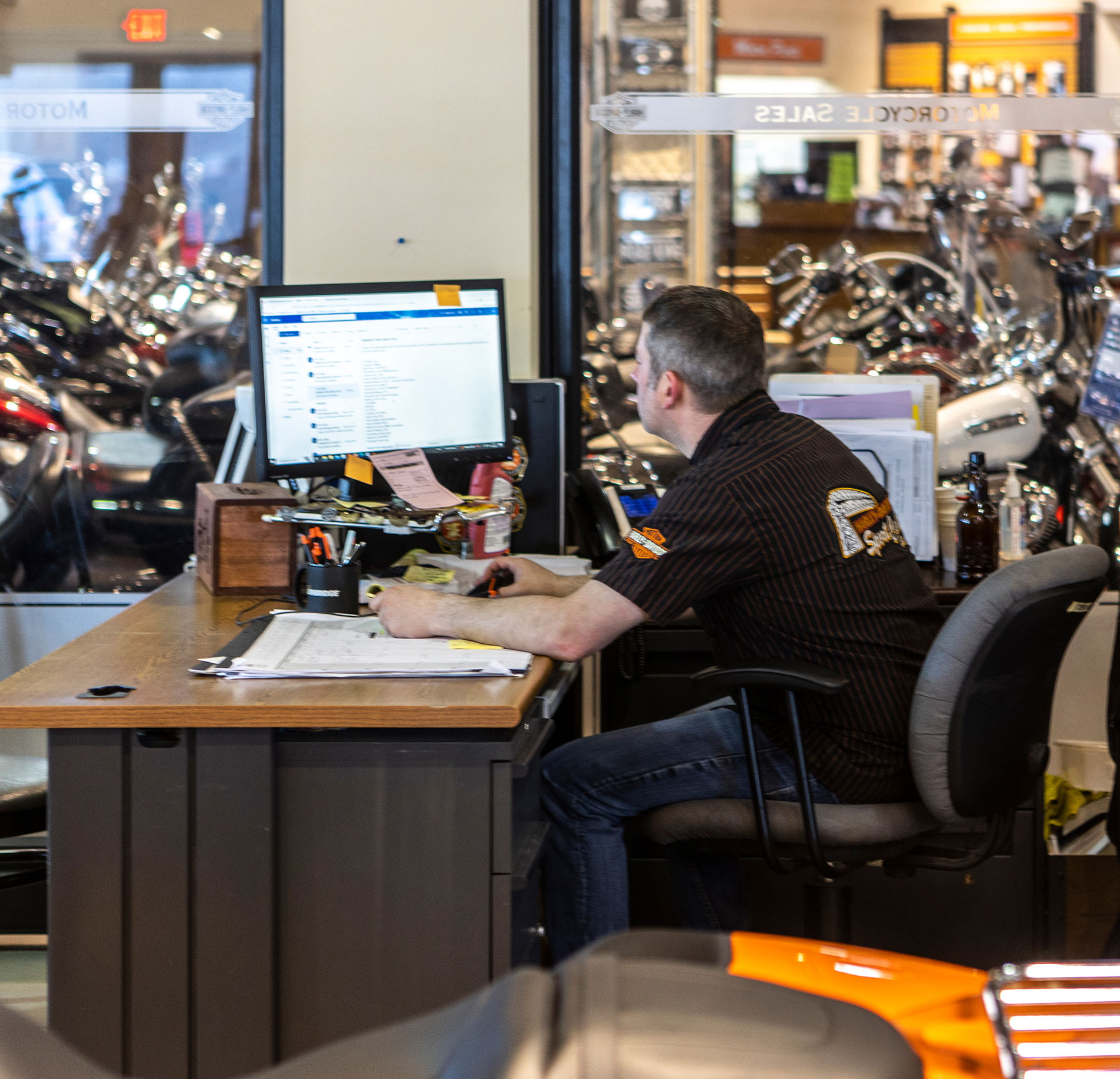 Zoomed out view of a man sitting at a desk in a motorcycle showroom