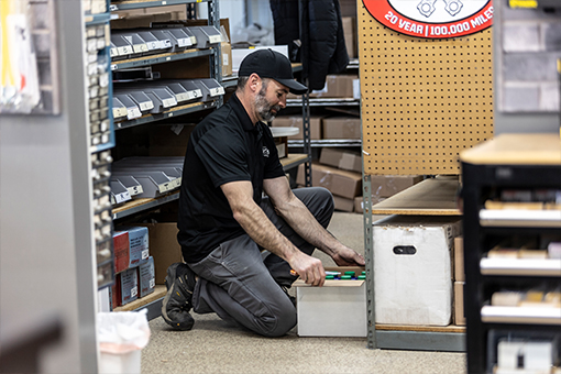 Image of a man kneeling down and looking through boxes of machine parts.