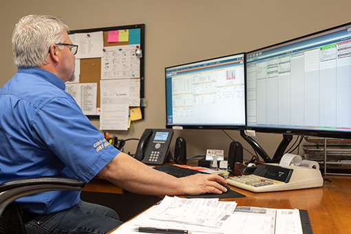 Image of a man working at a desk in front of two computer monitors.