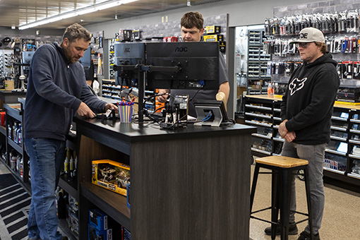 Image of one customer service employee and two customers at a checkout counter.