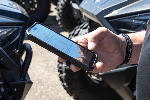 Image of a person holding a touchscreen cellphone in front of some vehicles.