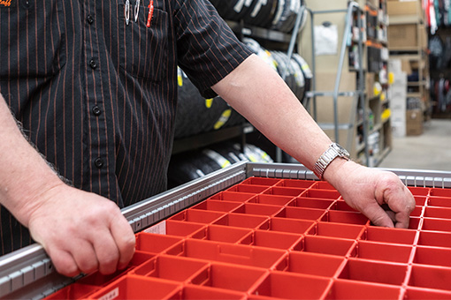 Image of a man sorting machine parts into a red grid box structure.